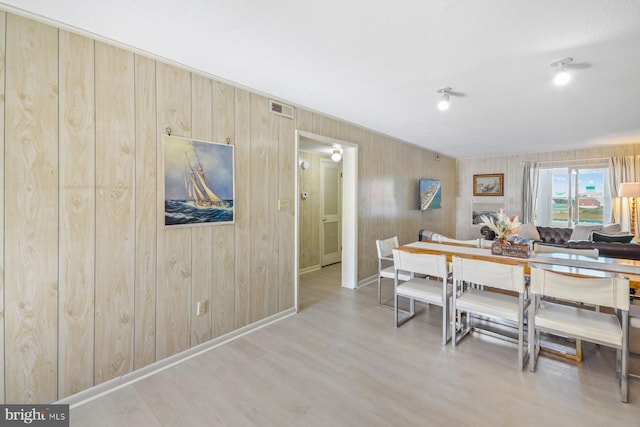 dining space featuring light wood-type flooring and wooden walls