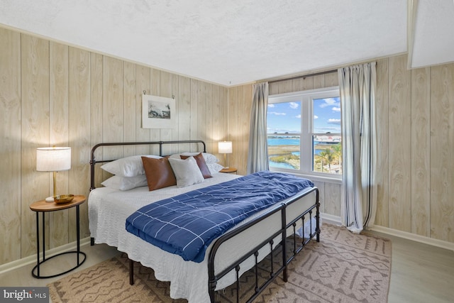 bedroom featuring a textured ceiling, wooden walls, and hardwood / wood-style floors