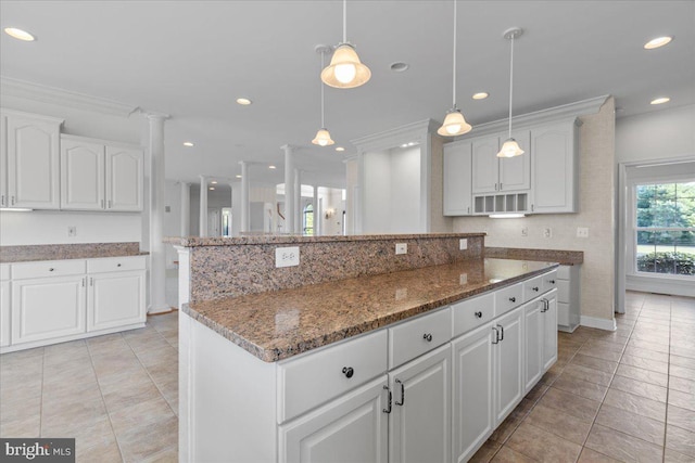 kitchen featuring dark stone countertops, white cabinetry, a center island, decorative light fixtures, and ornamental molding