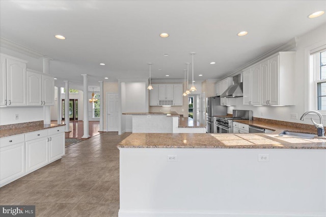 kitchen with white cabinets, sink, decorative light fixtures, stainless steel gas stove, and wall chimney range hood