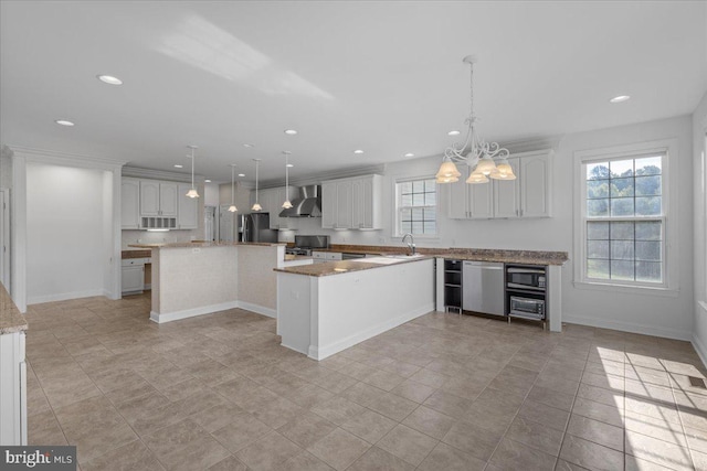 kitchen with decorative light fixtures, stainless steel appliances, wall chimney exhaust hood, and white cabinets