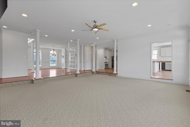 unfurnished living room featuring ceiling fan with notable chandelier, decorative columns, ornamental molding, and carpet