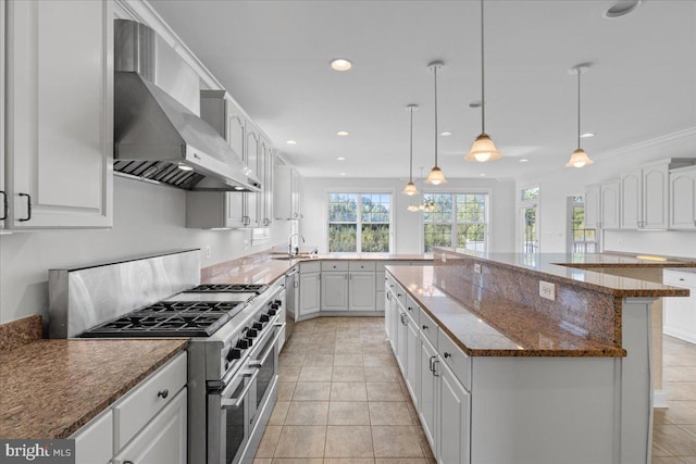 kitchen featuring white cabinets, decorative light fixtures, appliances with stainless steel finishes, and wall chimney range hood