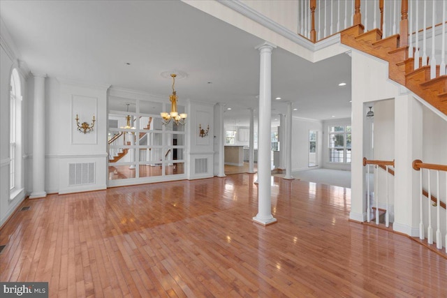 interior space featuring a notable chandelier, light wood-type flooring, crown molding, and ornate columns