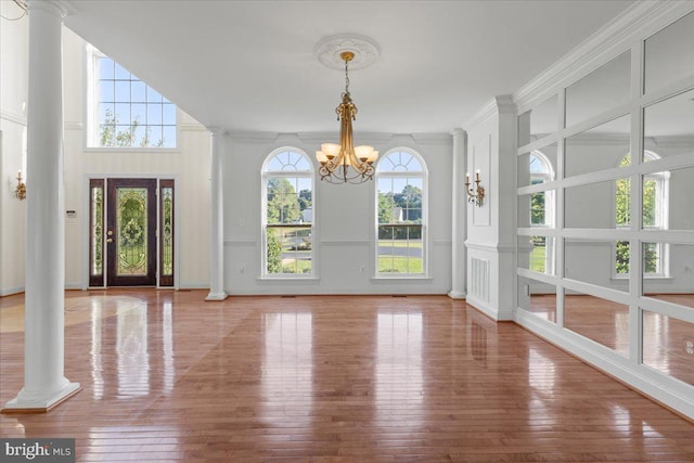 foyer entrance featuring wood-type flooring, an inviting chandelier, decorative columns, and ornamental molding