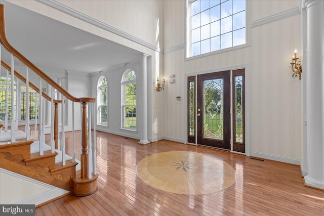 foyer with a high ceiling, light wood-type flooring, decorative columns, and a wealth of natural light