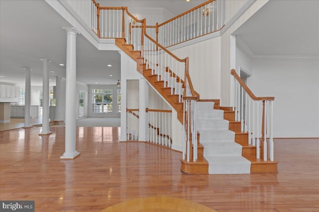 stairway featuring ornamental molding, wood-type flooring, a high ceiling, and ornate columns