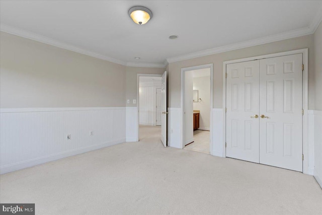 unfurnished bedroom featuring light colored carpet, a closet, crown molding, and connected bathroom