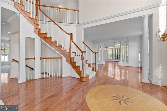 interior space with ornamental molding, a towering ceiling, hardwood / wood-style flooring, and ornate columns