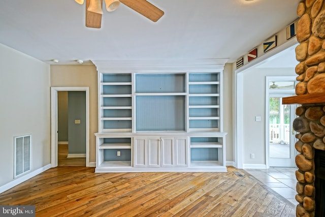 unfurnished living room with ceiling fan, hardwood / wood-style flooring, and a stone fireplace