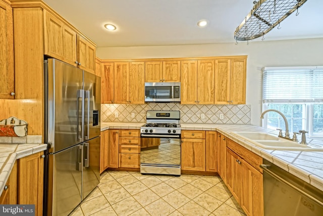 kitchen with light tile patterned floors, sink, appliances with stainless steel finishes, and tile countertops