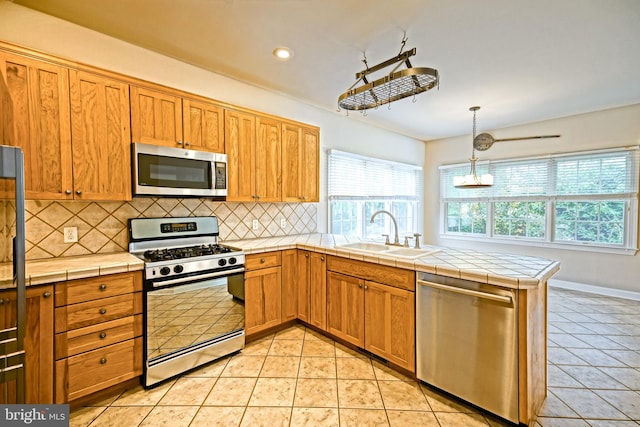 kitchen featuring appliances with stainless steel finishes, decorative backsplash, pendant lighting, tile counters, and sink