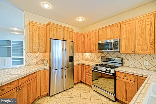 kitchen featuring tasteful backsplash, light tile patterned floors, stainless steel appliances, and tile countertops