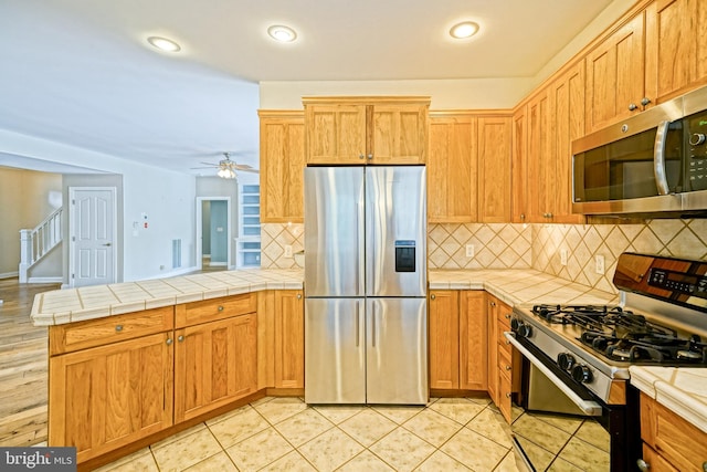 kitchen featuring backsplash, light tile patterned floors, stainless steel appliances, tile countertops, and ceiling fan