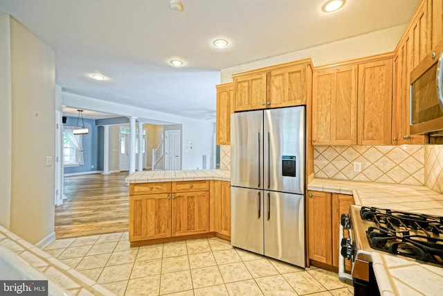 kitchen featuring pendant lighting, light tile patterned flooring, kitchen peninsula, tasteful backsplash, and stainless steel appliances