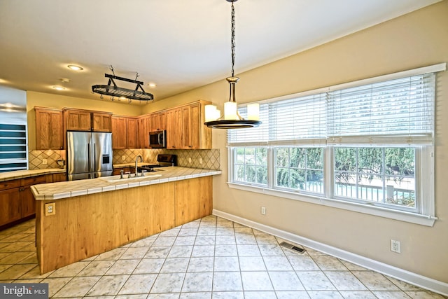 kitchen with appliances with stainless steel finishes, tile countertops, kitchen peninsula, and a wealth of natural light