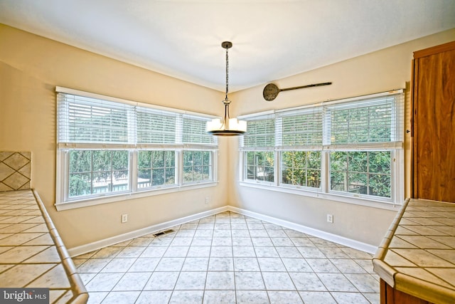 unfurnished dining area with a notable chandelier, light tile patterned flooring, and a healthy amount of sunlight