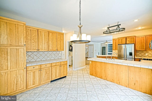 kitchen with appliances with stainless steel finishes, ceiling fan with notable chandelier, backsplash, tile countertops, and sink