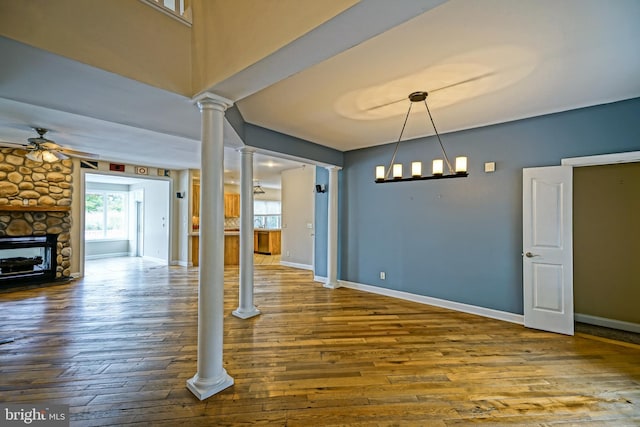 unfurnished dining area with decorative columns, a fireplace, hardwood / wood-style floors, and ceiling fan