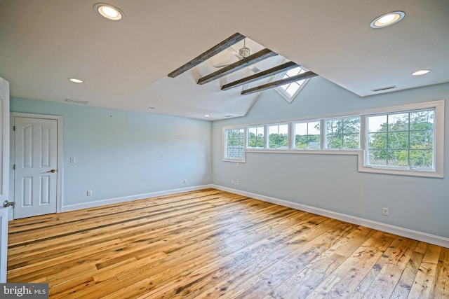 spare room with lofted ceiling with skylight and light hardwood / wood-style flooring