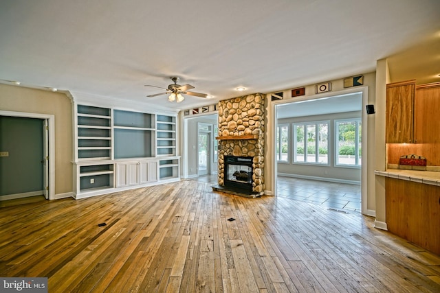 unfurnished living room featuring ceiling fan, a stone fireplace, and wood-type flooring