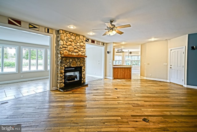 living room with ceiling fan, light hardwood / wood-style flooring, a fireplace, and a healthy amount of sunlight