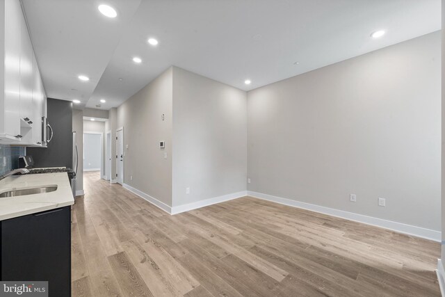 kitchen with light stone countertops, white cabinetry, sink, and light hardwood / wood-style flooring