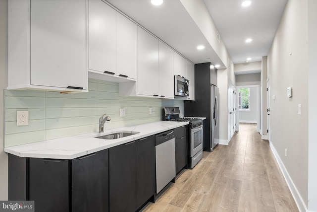 kitchen featuring white cabinets, light stone countertops, stainless steel appliances, light wood-type flooring, and sink