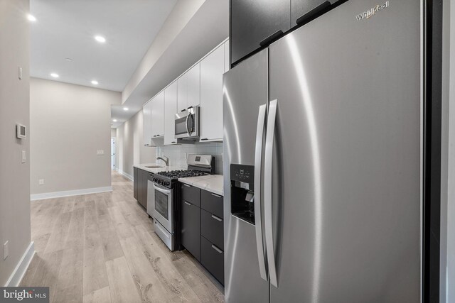 kitchen with appliances with stainless steel finishes, tasteful backsplash, white cabinets, light hardwood / wood-style flooring, and sink