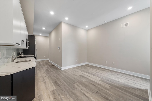 kitchen with decorative backsplash, light hardwood / wood-style floors, white cabinetry, light stone countertops, and sink