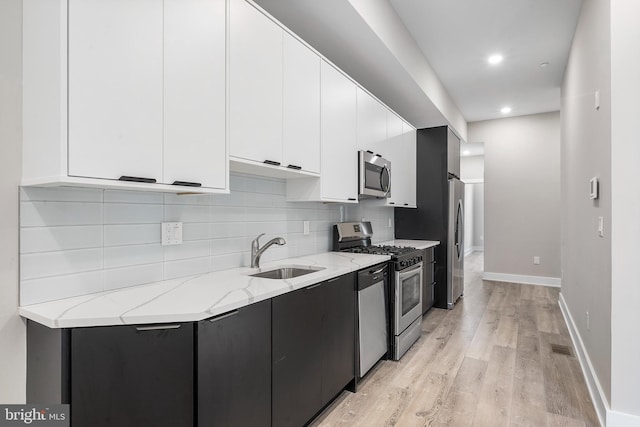 kitchen with appliances with stainless steel finishes, light hardwood / wood-style floors, white cabinetry, light stone countertops, and sink