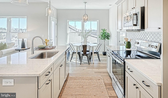 kitchen with sink, hanging light fixtures, appliances with stainless steel finishes, a kitchen island with sink, and white cabinets