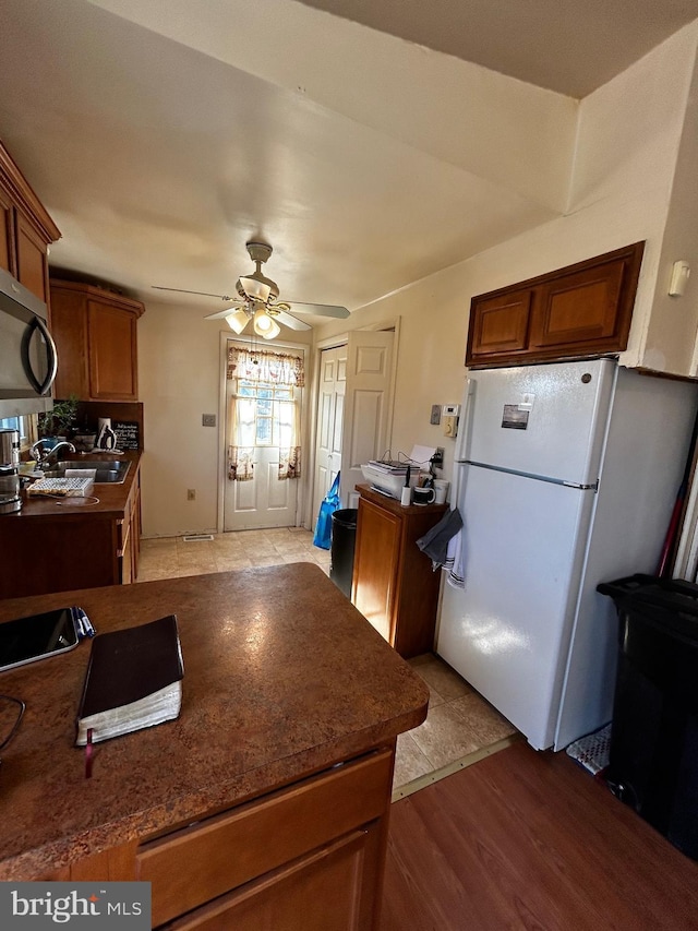 kitchen with dark countertops, stainless steel microwave, a ceiling fan, freestanding refrigerator, and a sink