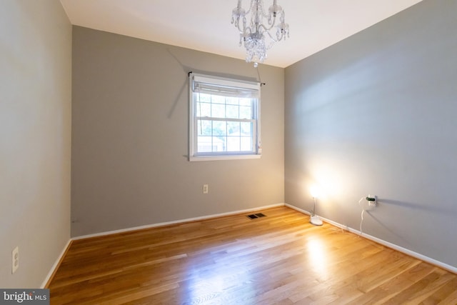 unfurnished room featuring a notable chandelier and hardwood / wood-style floors