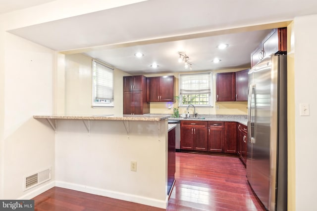 kitchen with stainless steel fridge, dark hardwood / wood-style flooring, light stone countertops, kitchen peninsula, and a kitchen bar