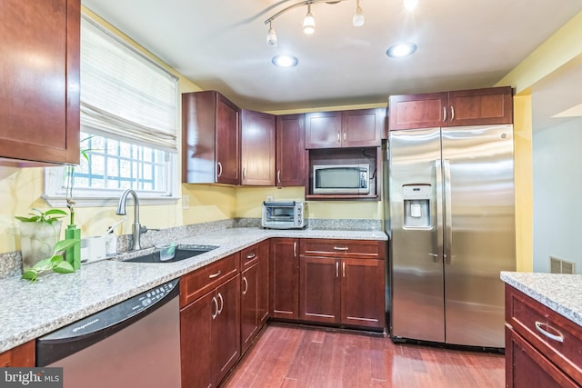 kitchen featuring stainless steel appliances, light stone countertops, dark wood-type flooring, and sink