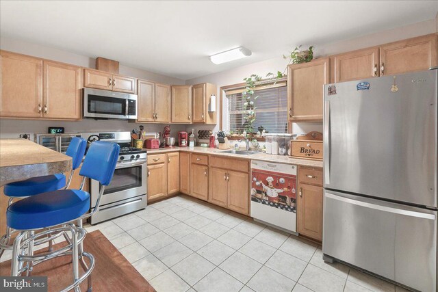 kitchen with light brown cabinetry, light tile patterned flooring, sink, and stainless steel appliances