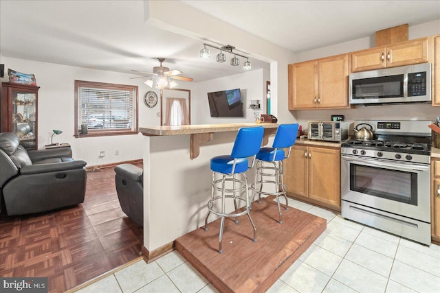 kitchen with ceiling fan, a breakfast bar area, appliances with stainless steel finishes, and kitchen peninsula