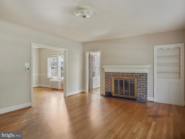 unfurnished living room with radiator, hardwood / wood-style floors, built in features, and a brick fireplace