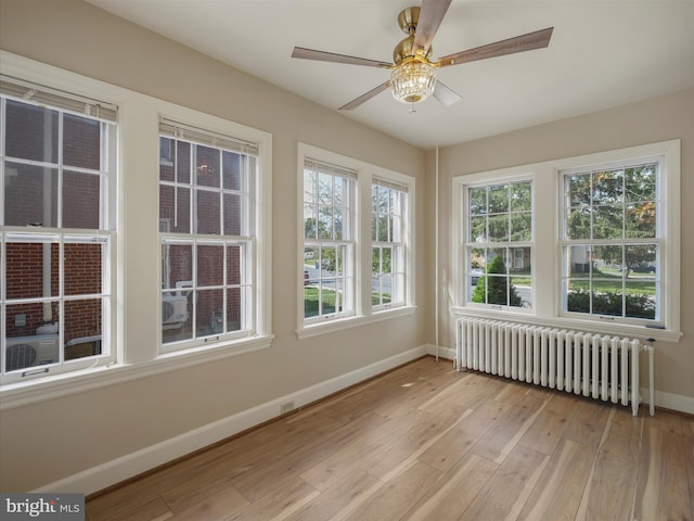 unfurnished sunroom featuring ceiling fan, radiator heating unit, and plenty of natural light