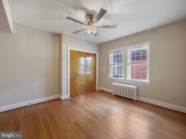 unfurnished bedroom featuring ceiling fan, radiator heating unit, a closet, and light hardwood / wood-style flooring