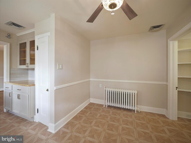 empty room with light parquet floors, ceiling fan, and radiator heating unit