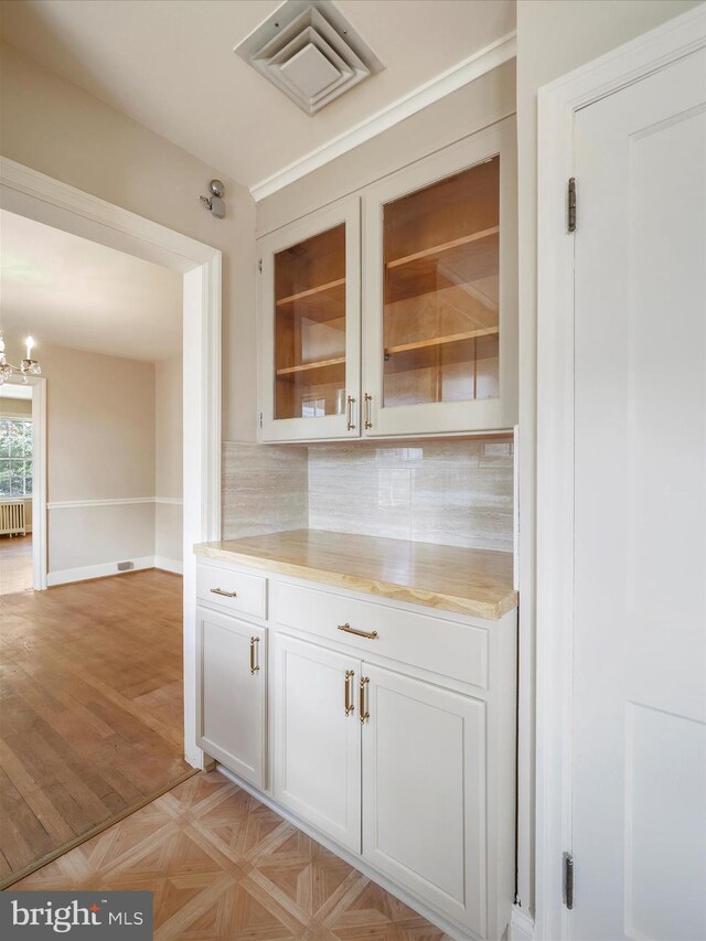 bar with a chandelier, tasteful backsplash, white cabinets, light parquet flooring, and radiator heating unit