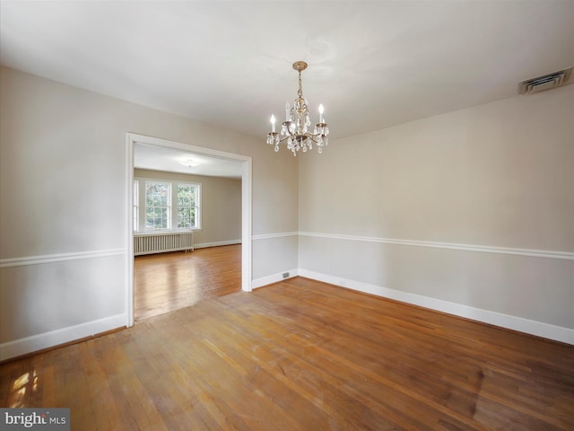 unfurnished room with wood-type flooring, an inviting chandelier, and radiator heating unit