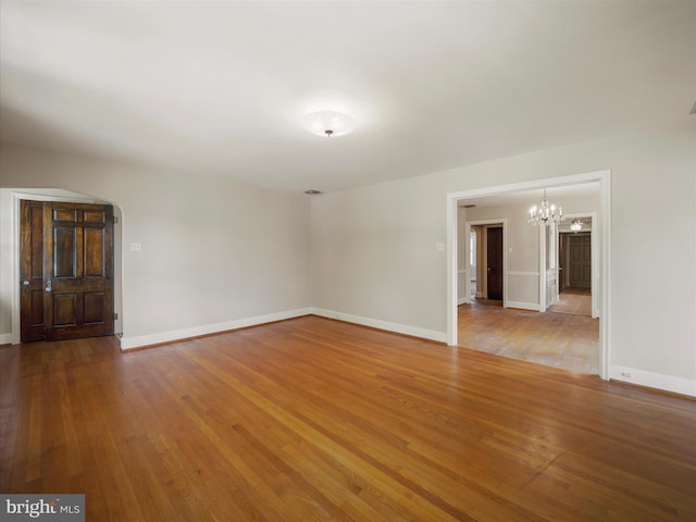 spare room featuring wood-type flooring and a chandelier