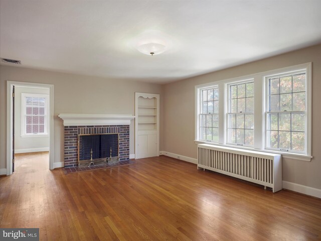 unfurnished living room featuring radiator heating unit, wood-type flooring, and a brick fireplace