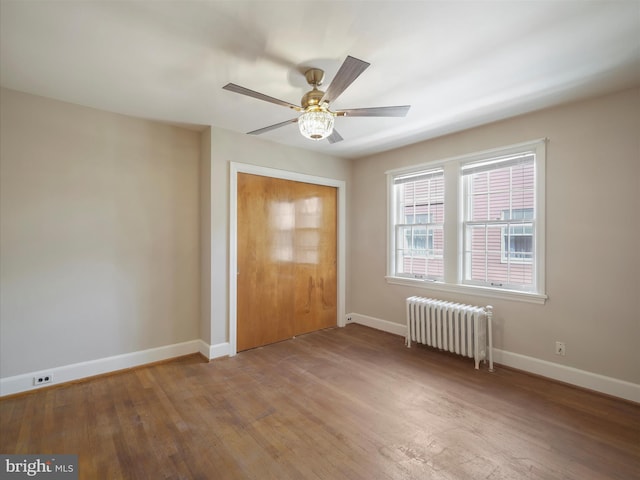 unfurnished bedroom with radiator heating unit, a closet, ceiling fan, and hardwood / wood-style flooring