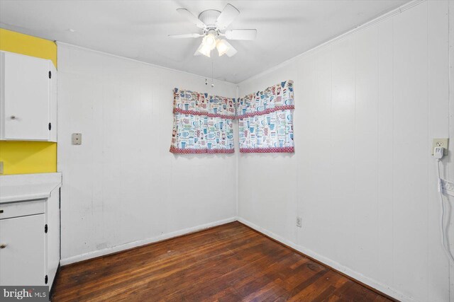 unfurnished room with wooden walls, ceiling fan, dark wood-type flooring, and crown molding