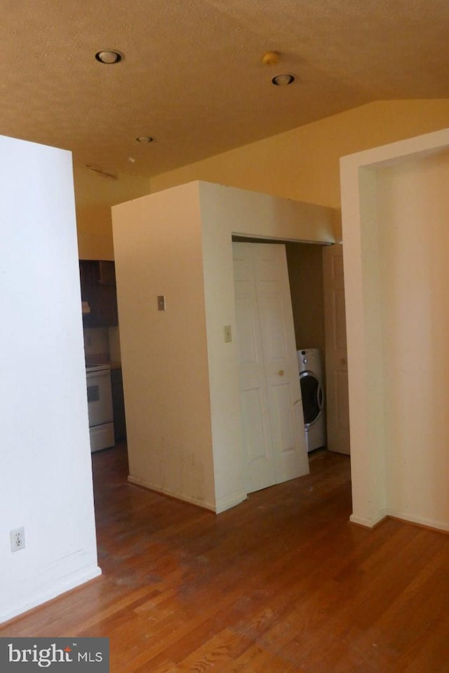 empty room with wood-type flooring, washer / clothes dryer, a textured ceiling, and vaulted ceiling