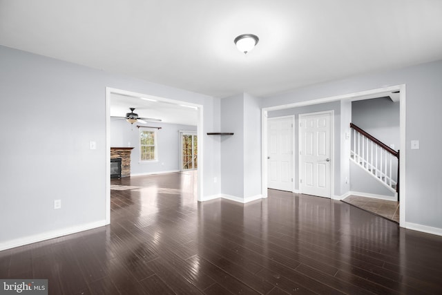 unfurnished living room featuring dark hardwood / wood-style flooring, a stone fireplace, and ceiling fan